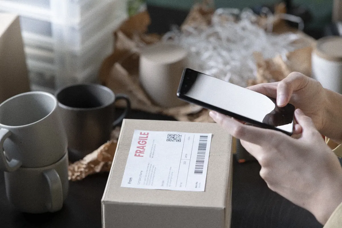 Online store owner checking an order on her phone beside a labelled parcel: post-purchase email flow for a Shopify store