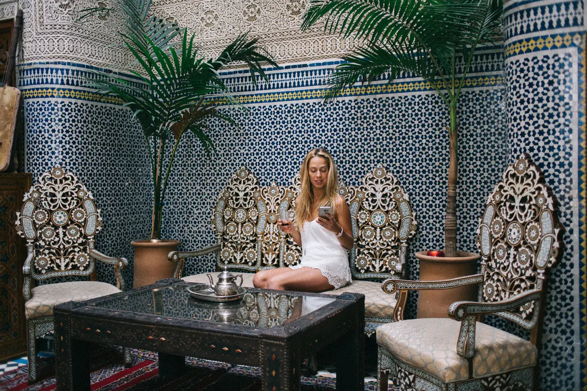 Guest relaxing in a zellige-tiled Moroccan lounge with carved chairs: hospitality photography for a riad or boutique hotel