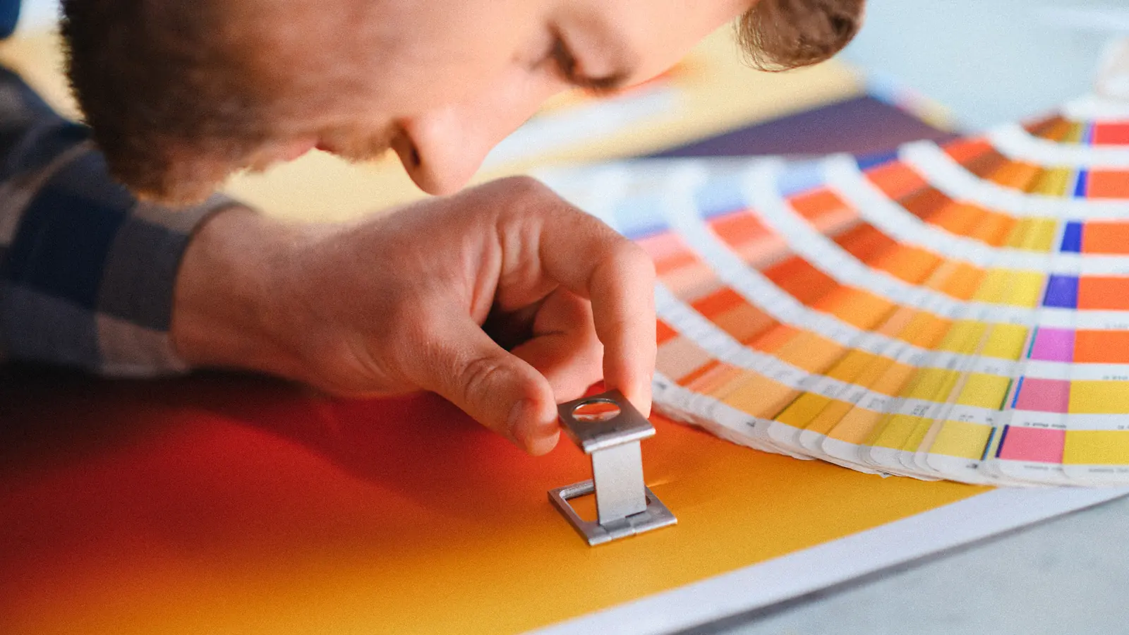 Graphiste contrôlant une couleur à la loupe sur un nuancier : logo, charte graphique et identité visuelle