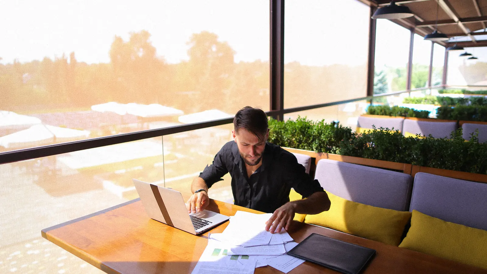 Entrepreneur relisant des documents près de son ordinateur portable en terrasse : comprendre le prix et le devis d’un site internet