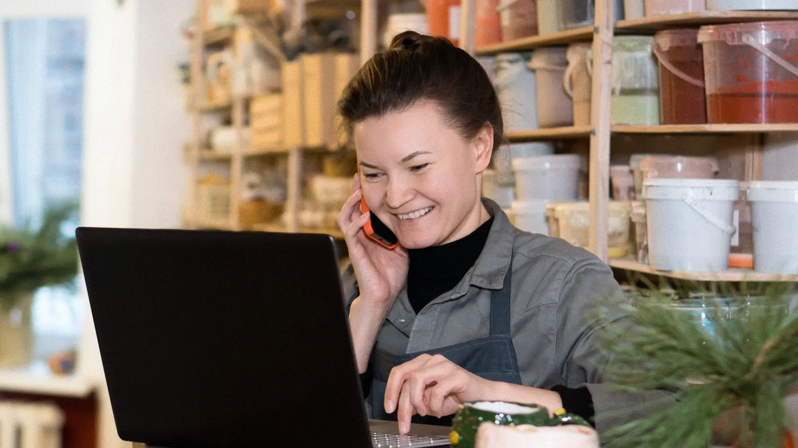 Artisane souriante au téléphone devant son ordinateur portable dans son atelier : créer un site internet pas cher pour son activité