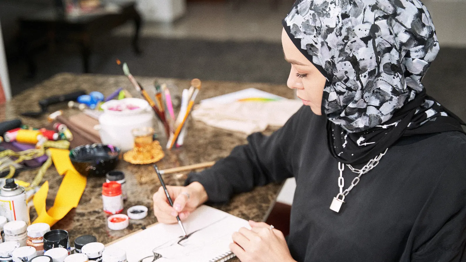 مصممة ترسم بيدها في الاستوديو بين الألوان والفرش: ما لا يفعله تصميم شعار بالذكاء الاصطناعي