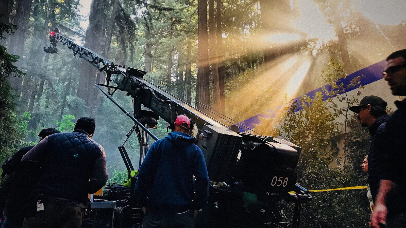Équipe de tournage installant une caméra sur grue en forêt, dans les rayons du soleil : production d’une vidéo publicitaire