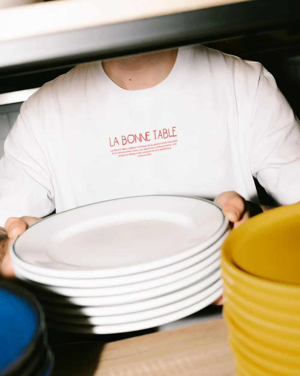 Waiter carrying plates in a white La Bonne Table t-shirt