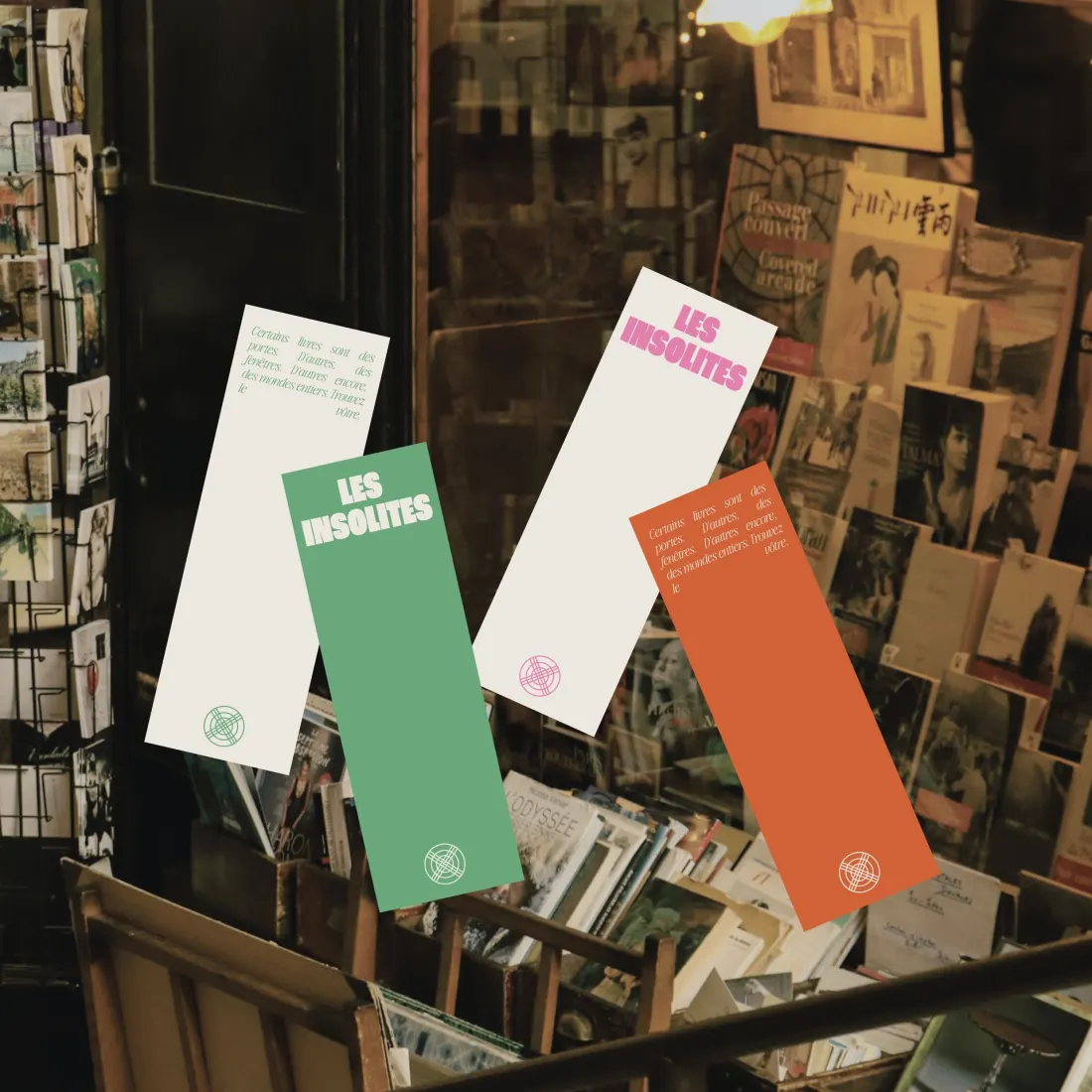 Les Insolites bookmarks in pink, green and orange over a wall of postcards