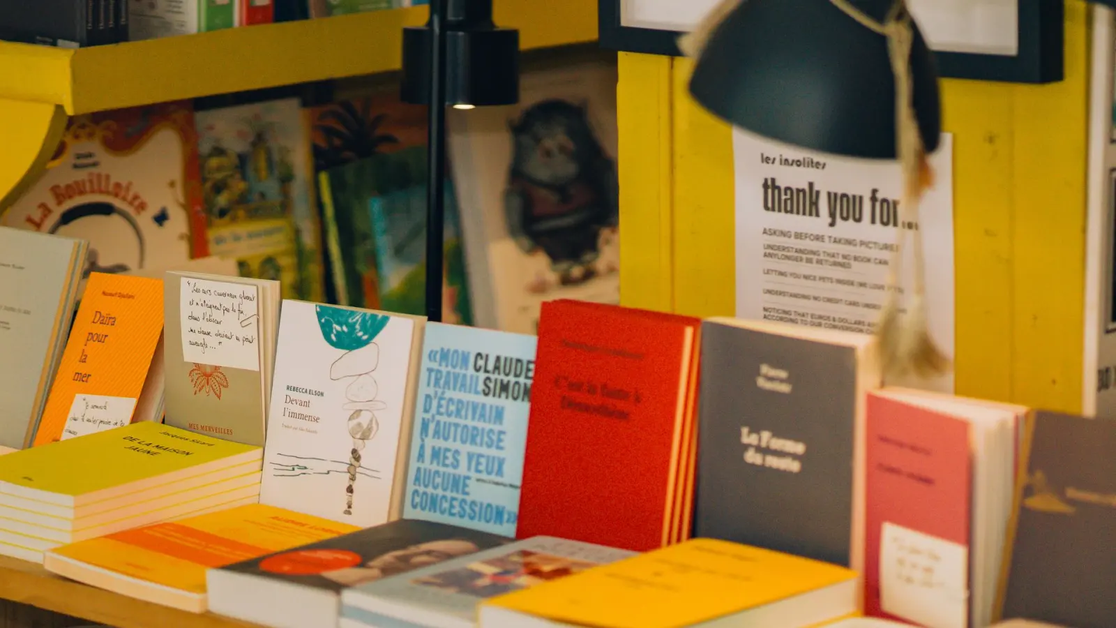 Books displayed on a wooden table against yellow walls in Les Insolites