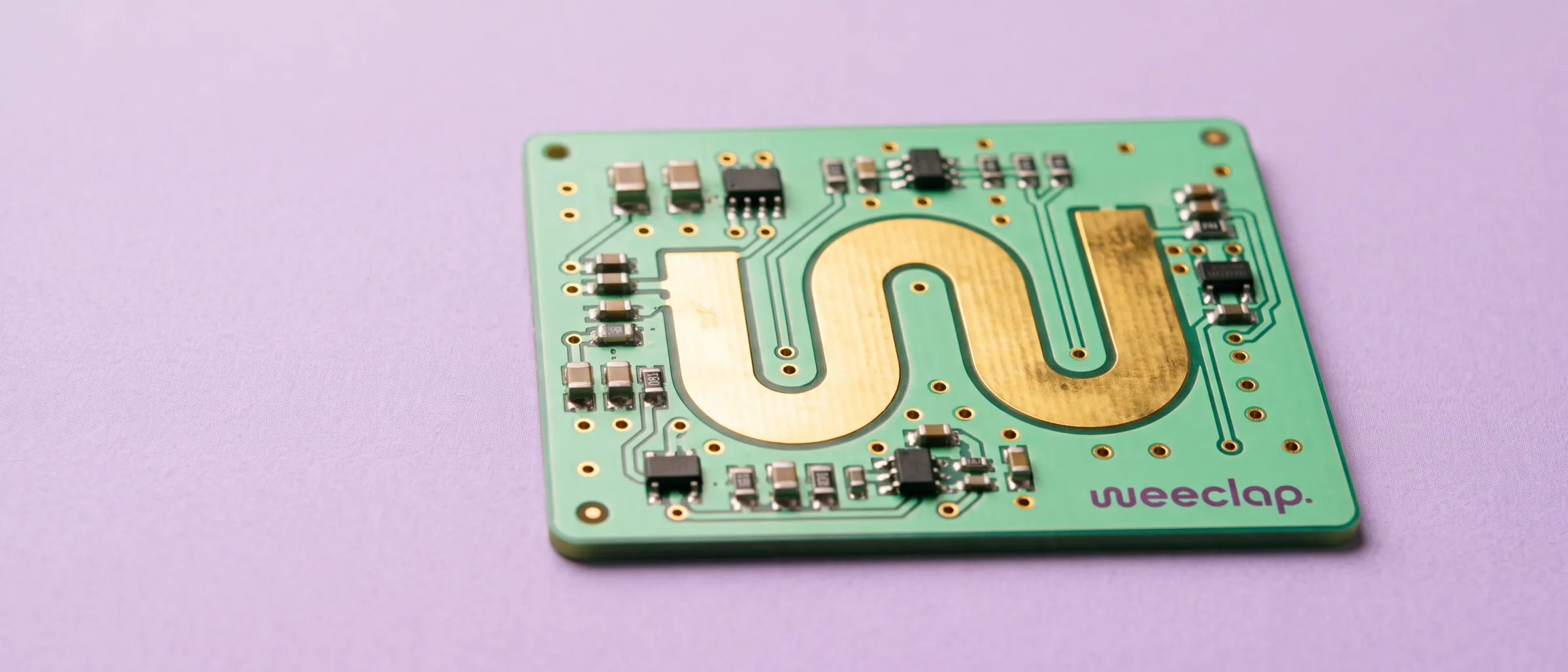 Mint circuit board whose gold trace draws the W monogram, the weeclap wordmark printed in the corner, on lilac