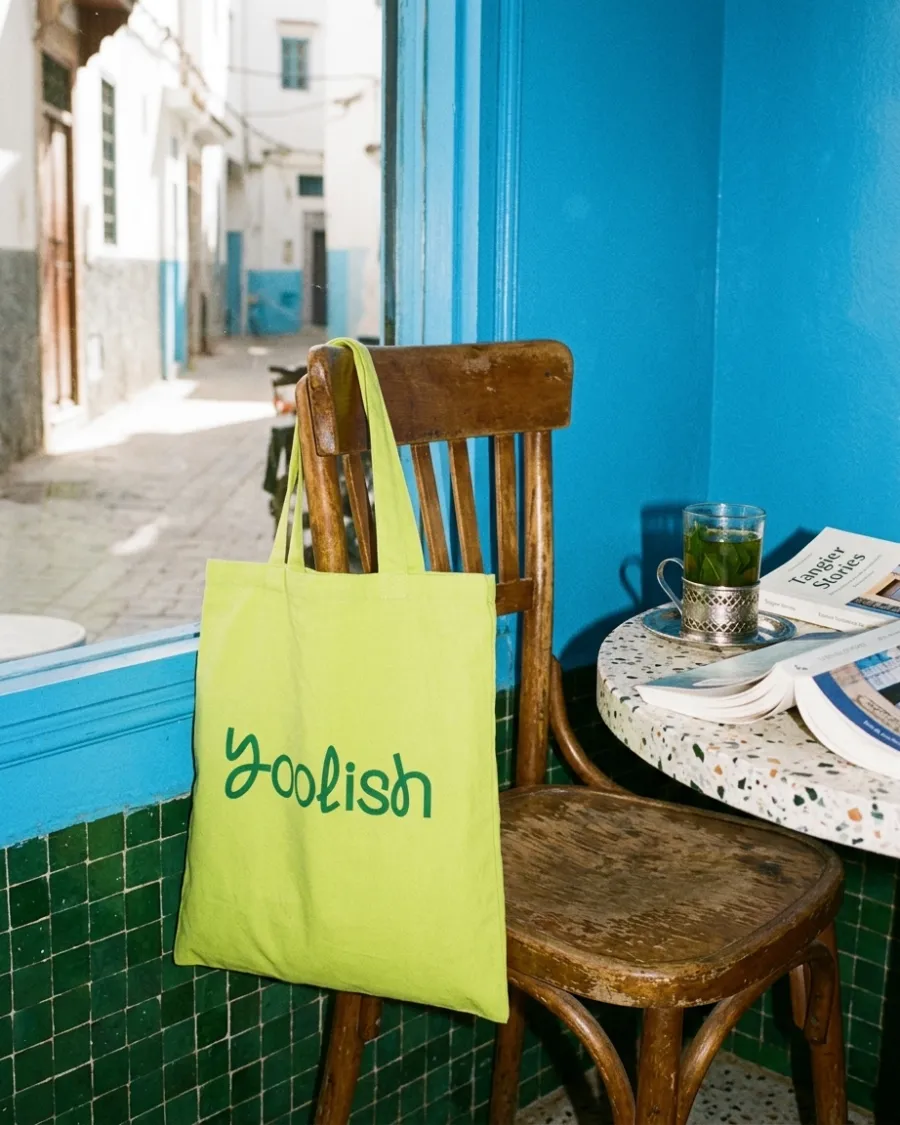 Lime tote bag with the Yoolish wordmark on a chair in a blue café in Tangier